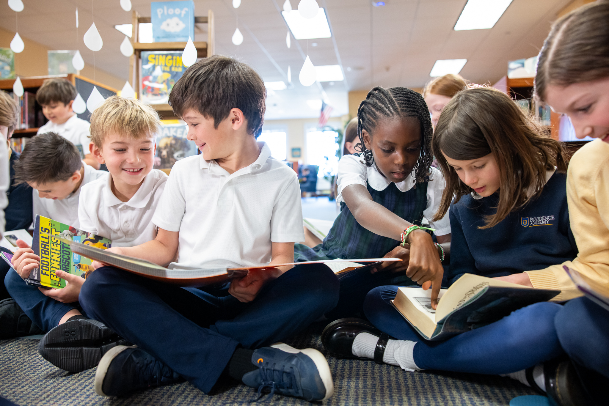 Lower School students sitting cross-legged on the library floor, reading together and pointing out pages to one another.